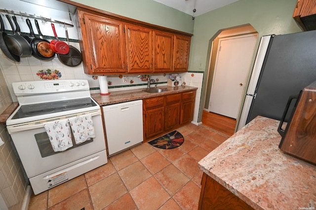 kitchen featuring decorative backsplash, white appliances, light stone countertops, and sink