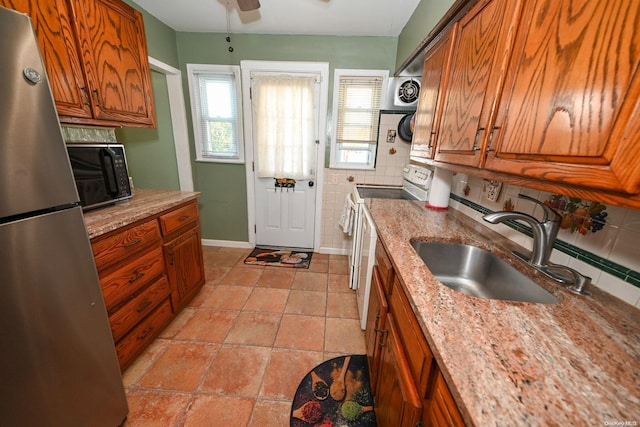 kitchen with light stone countertops, sink, ceiling fan, stainless steel appliances, and backsplash