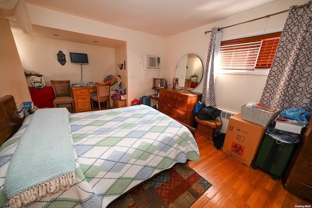 bedroom with a wall mounted air conditioner, wood-type flooring, and multiple windows