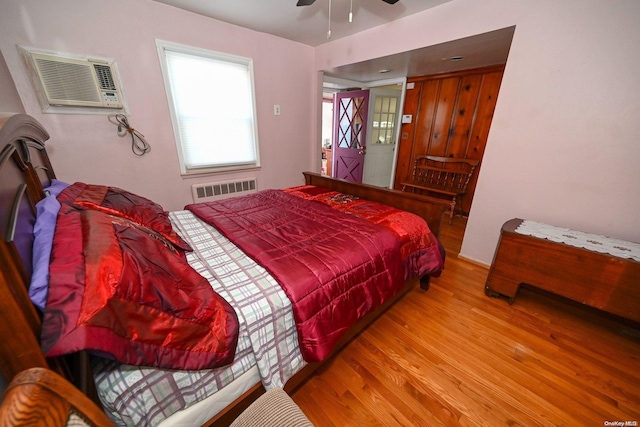 bedroom with hardwood / wood-style floors, ceiling fan, an AC wall unit, and radiator