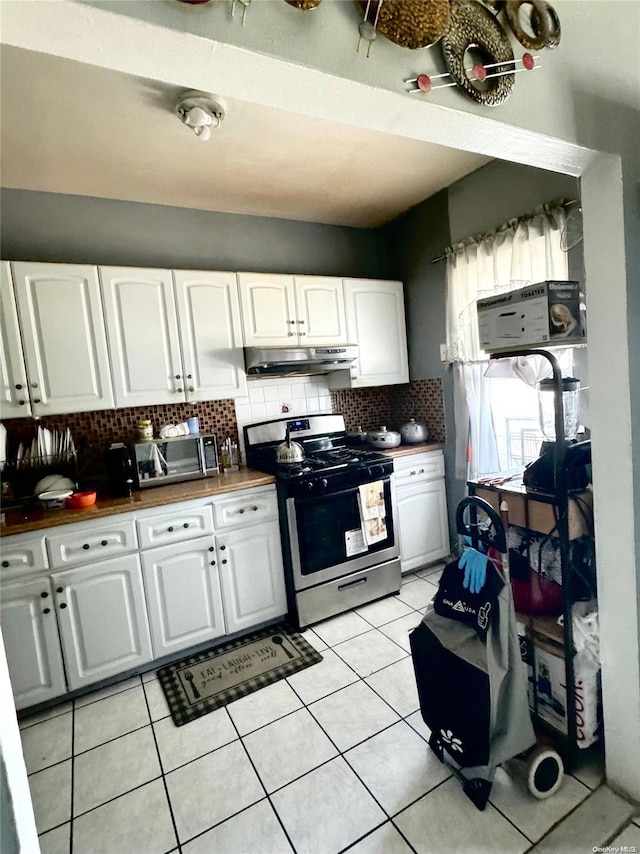 kitchen with wood counters, backsplash, white cabinets, light tile patterned floors, and stainless steel range oven