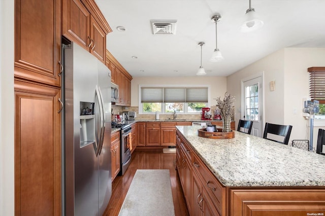 kitchen with a wealth of natural light, a center island, pendant lighting, and appliances with stainless steel finishes