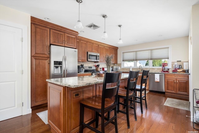 kitchen with light stone countertops, stainless steel appliances, dark hardwood / wood-style flooring, pendant lighting, and a kitchen island