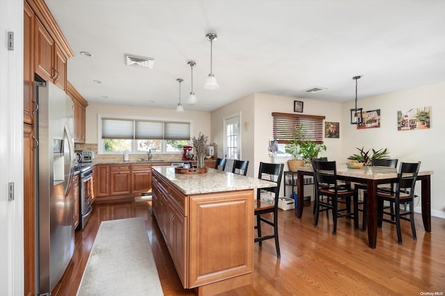 kitchen featuring stainless steel appliances, pendant lighting, hardwood / wood-style flooring, a kitchen island, and a breakfast bar area