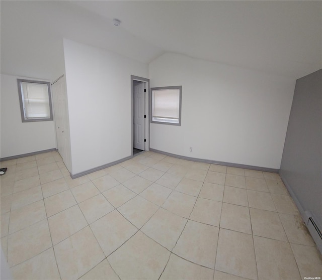 tiled empty room with a baseboard heating unit and lofted ceiling