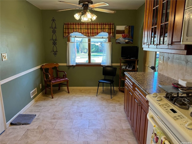 kitchen featuring light tile patterned floors, backsplash, ceiling fan, and white gas stove