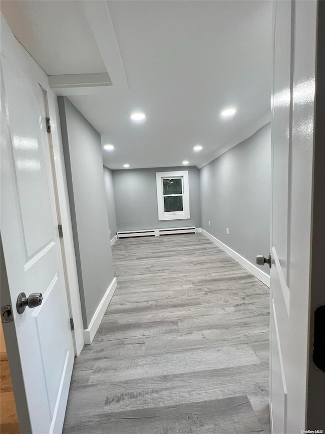 basement featuring light wood-type flooring and a baseboard radiator