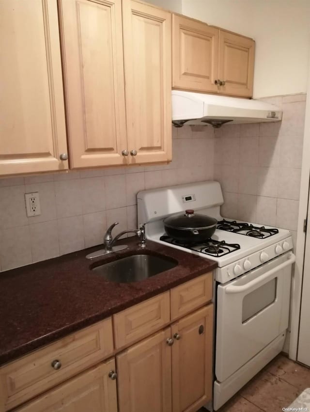 kitchen featuring backsplash, dark stone countertops, white gas range, and sink