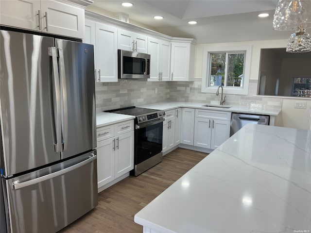 kitchen with sink, hanging light fixtures, stainless steel appliances, hardwood / wood-style floors, and white cabinets