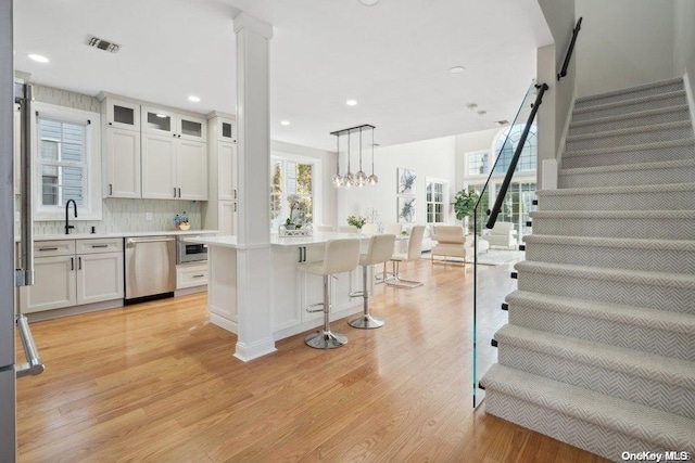 kitchen featuring white cabinets, decorative backsplash, appliances with stainless steel finishes, decorative light fixtures, and light hardwood / wood-style floors