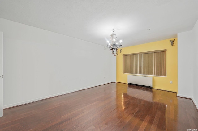 spare room with radiator, a chandelier, and dark wood-type flooring