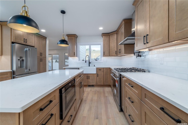 kitchen with high end appliances, sink, hanging light fixtures, tasteful backsplash, and light hardwood / wood-style floors