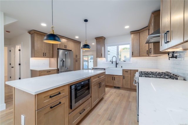 kitchen with white gas stove, wall chimney exhaust hood, hanging light fixtures, light hardwood / wood-style floors, and high quality fridge