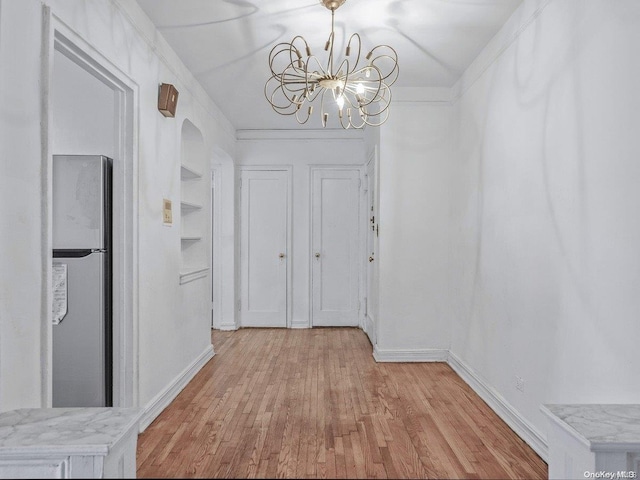 hallway featuring built in shelves, ornamental molding, light hardwood / wood-style floors, and a notable chandelier