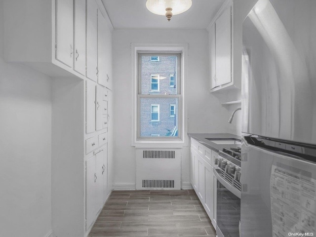 kitchen featuring radiator, white cabinetry, high end stainless steel range oven, light hardwood / wood-style flooring, and white refrigerator