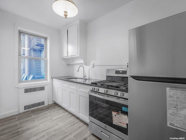 kitchen featuring radiator, white cabinets, sink, light wood-type flooring, and stainless steel appliances