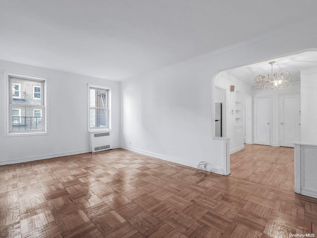 spare room with light parquet floors, radiator, and an inviting chandelier