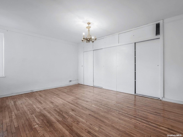 unfurnished bedroom with hardwood / wood-style flooring, a chandelier, crown molding, and a closet