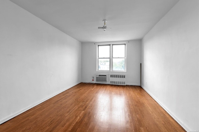 empty room featuring hardwood / wood-style flooring, ceiling fan, a wall mounted air conditioner, and radiator