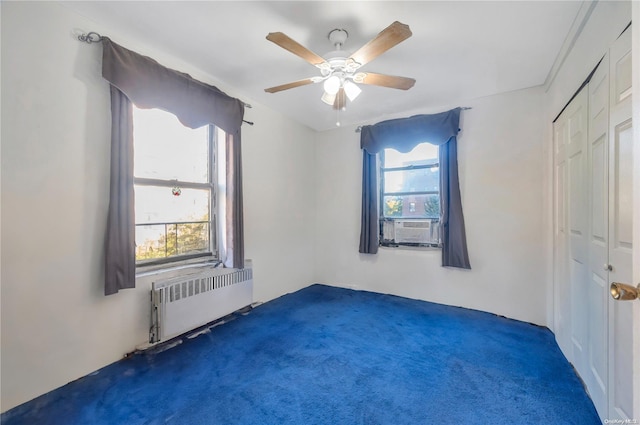 carpeted spare room featuring ceiling fan, cooling unit, radiator heating unit, and a wealth of natural light