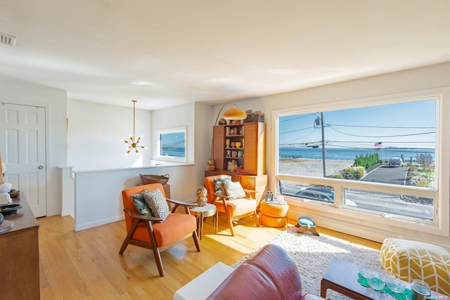 sitting room featuring a notable chandelier, a water view, and light hardwood / wood-style flooring