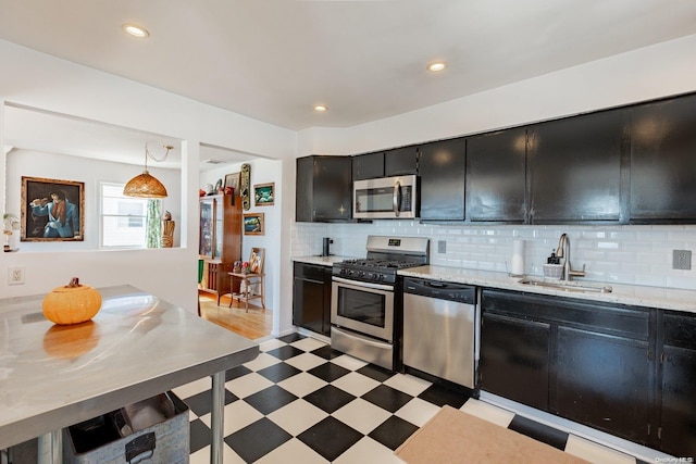 kitchen featuring light stone countertops, appliances with stainless steel finishes, tasteful backsplash, sink, and pendant lighting