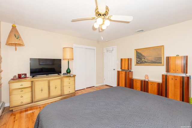 bedroom with ceiling fan, light hardwood / wood-style floors, a baseboard radiator, and a closet