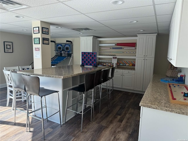 kitchen with a drop ceiling, stone counters, dark hardwood / wood-style floors, white cabinetry, and a breakfast bar area