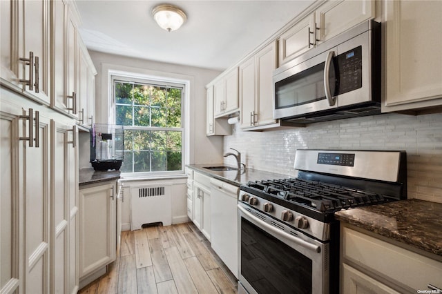 kitchen featuring dark stone counters, sink, light wood-type flooring, radiator heating unit, and stainless steel appliances