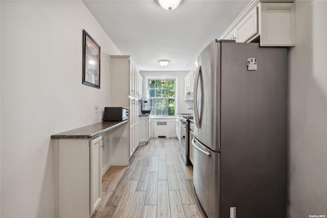 kitchen featuring white cabinets, light wood-type flooring, stainless steel appliances, and dark stone counters