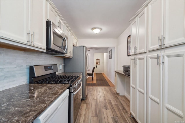 kitchen with dark stone counters, light hardwood / wood-style flooring, tasteful backsplash, white cabinetry, and stainless steel appliances