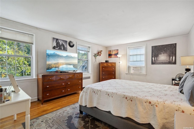 bedroom featuring hardwood / wood-style flooring, cooling unit, radiator, and multiple windows