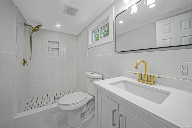 bathroom featuring a tile shower, vanity, tile walls, and toilet