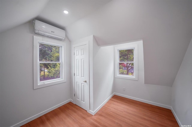 additional living space with an AC wall unit, plenty of natural light, wood-type flooring, and vaulted ceiling