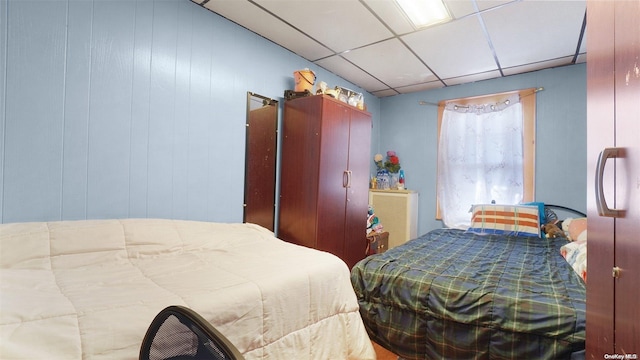 bedroom with a paneled ceiling and wood walls