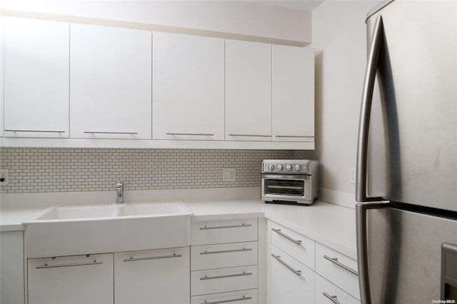 kitchen featuring white cabinetry, backsplash, and stainless steel refrigerator