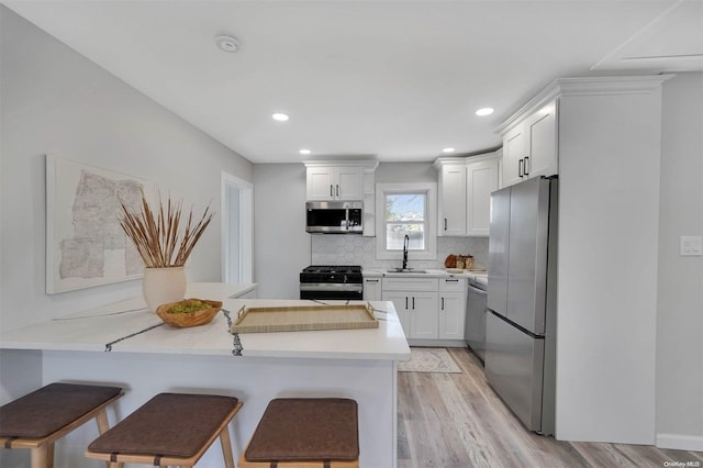 kitchen with white cabinetry, a breakfast bar, stainless steel appliances, and light wood-type flooring