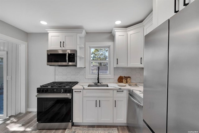 kitchen featuring white cabinetry, sink, stainless steel appliances, light hardwood / wood-style flooring, and backsplash