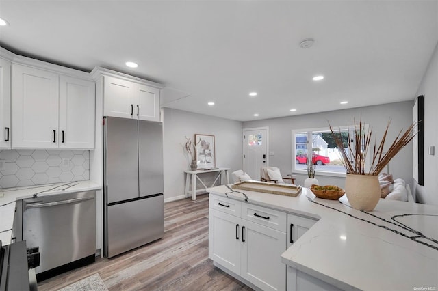 kitchen featuring light stone countertops, tasteful backsplash, stainless steel appliances, light hardwood / wood-style floors, and white cabinetry