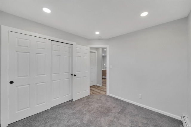 unfurnished bedroom featuring carpet flooring, a closet, and a baseboard heating unit