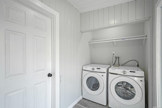 laundry area featuring separate washer and dryer, light hardwood / wood-style floors, and wood walls