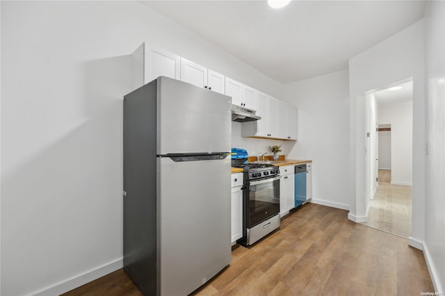 kitchen with light wood-type flooring, wood counters, stainless steel appliances, and white cabinetry