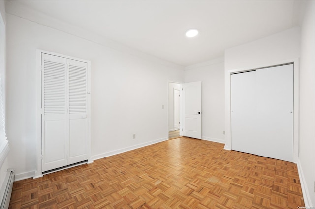 unfurnished bedroom with light parquet flooring, a baseboard heating unit, and two closets