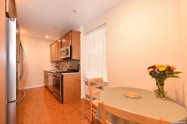 kitchen with appliances with stainless steel finishes, light hardwood / wood-style floors, tasteful backsplash, and radiator