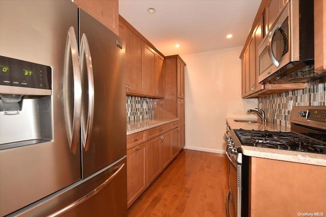 kitchen with backsplash, light hardwood / wood-style flooring, stainless steel appliances, and sink