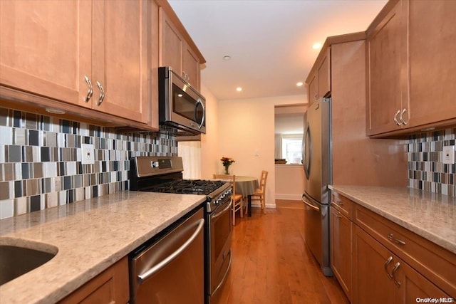 kitchen with backsplash, light stone counters, stainless steel appliances, sink, and light hardwood / wood-style flooring