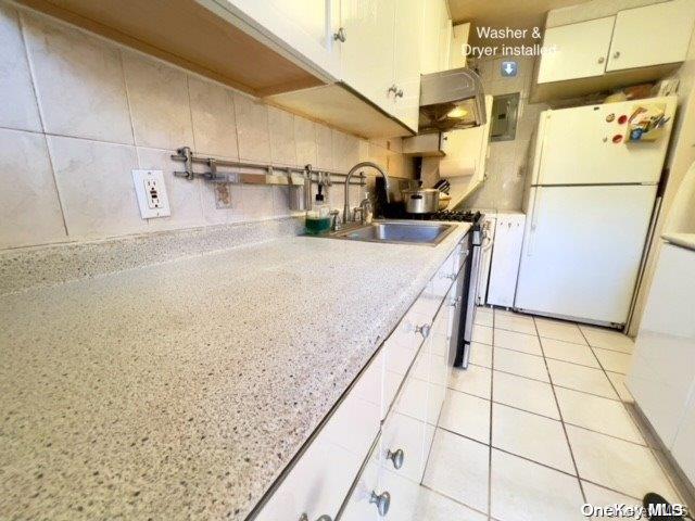 kitchen featuring sink, light tile patterned floors, white refrigerator, white cabinets, and electric panel