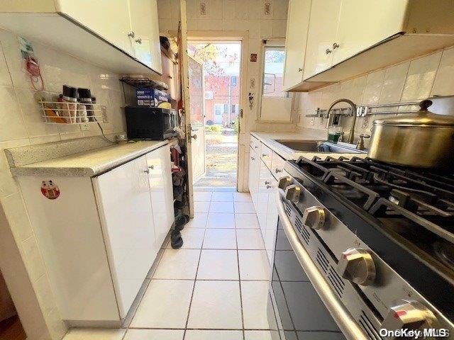 kitchen featuring gas stove, tasteful backsplash, sink, and white cabinets