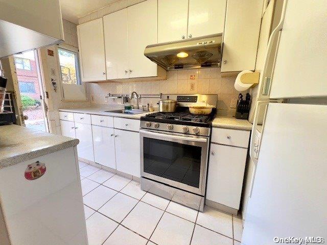 kitchen with decorative backsplash, sink, white refrigerator, white cabinets, and stainless steel gas stove