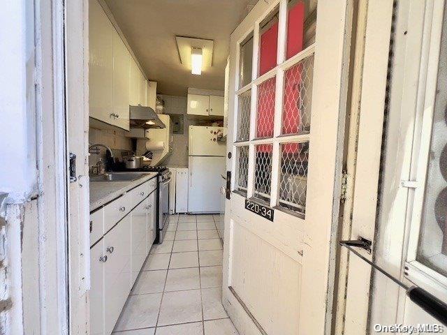 kitchen with white cabinetry, white fridge, stainless steel electric stove, light tile patterned floors, and exhaust hood